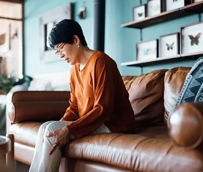 a distraught senior asian woman feeling unwell suffering from pain in leg while sitting on